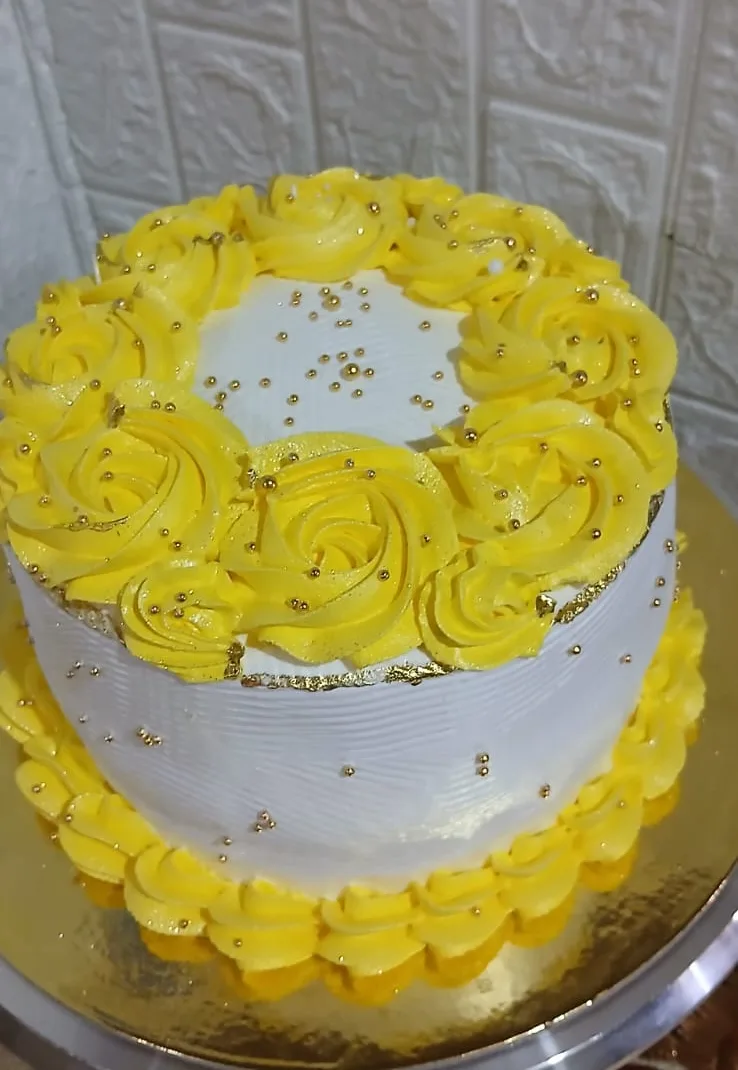 Queque blanco con una corona de rosetones amarillos y perlas doradas