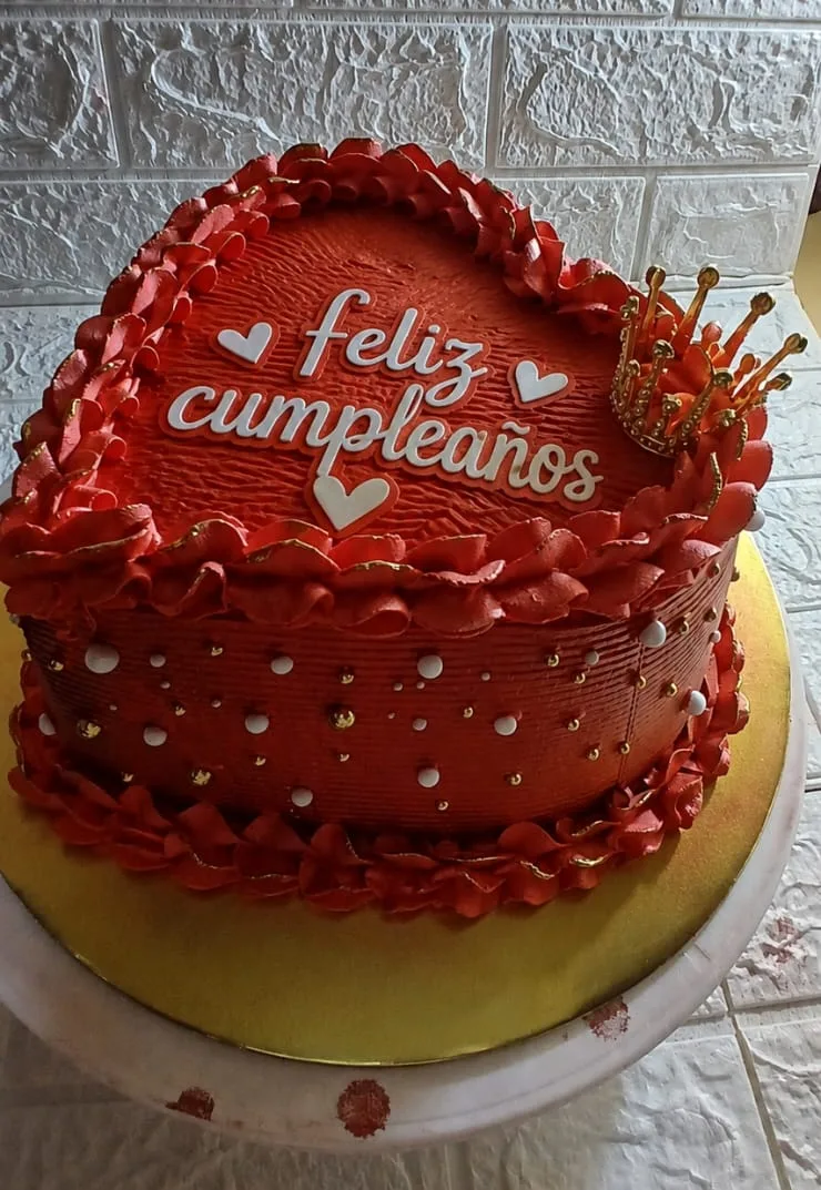 Queque rojo en forma de corazón con letrero de feliz cumpleaños, perlas blancas y una corona dorada