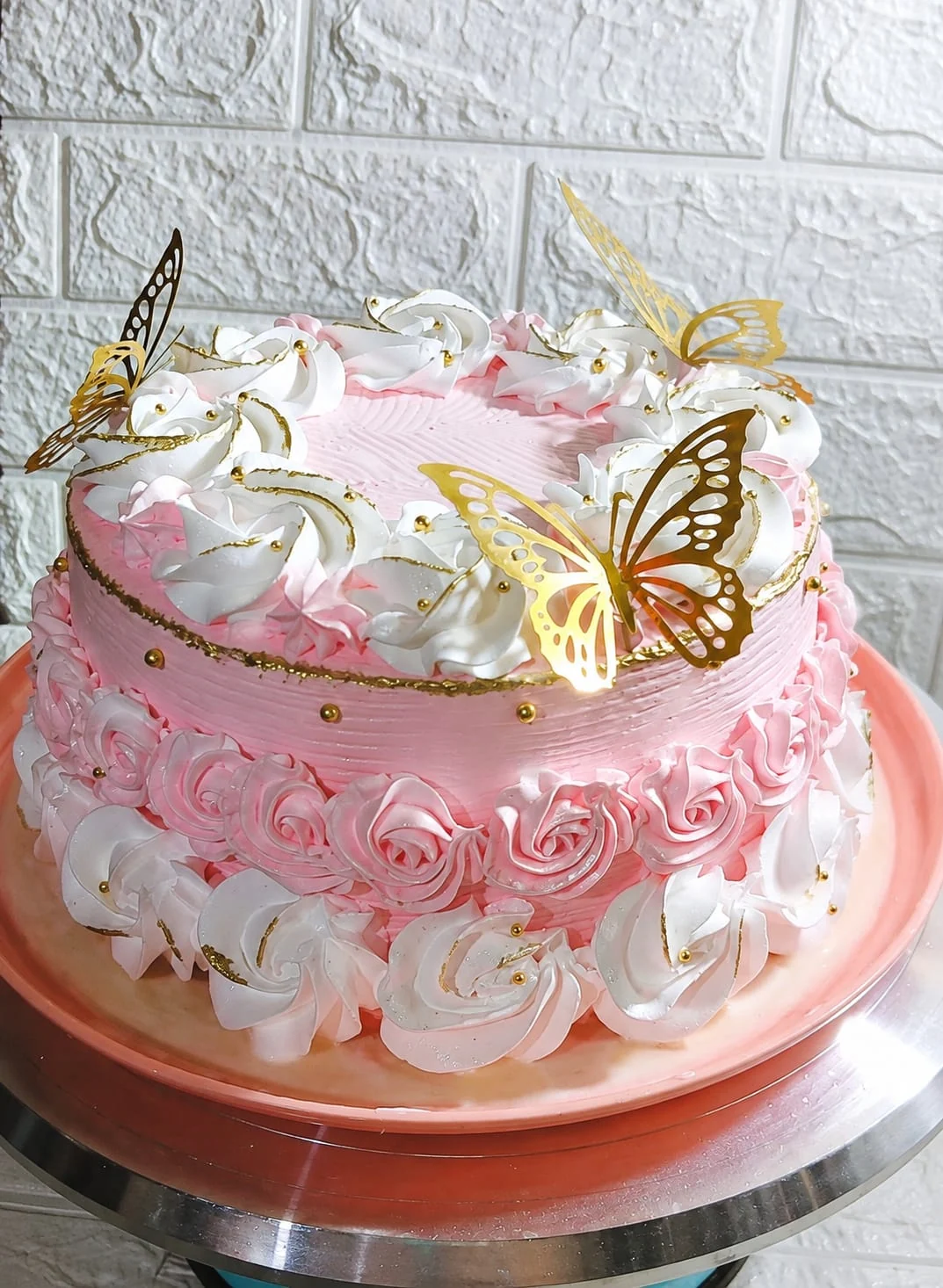 Queque rosa con decoración blanca y mariposas doradas