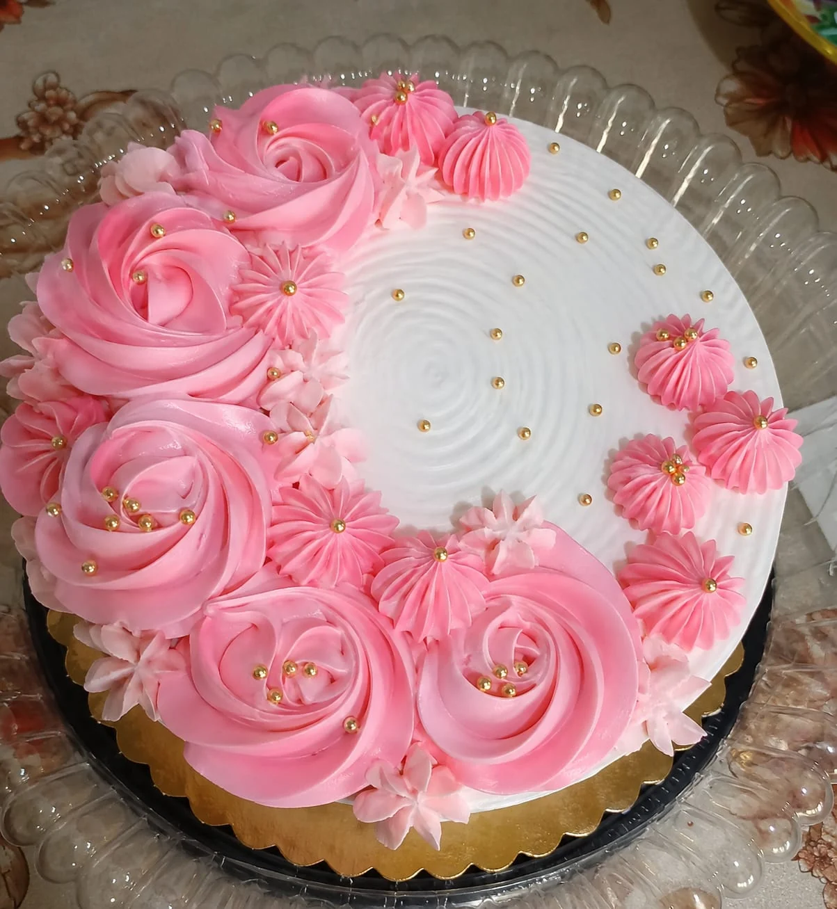 Queque redondo con rosetones rosados, decoración blanca y pequeñas perlas